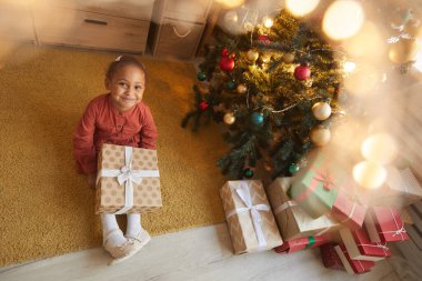 Noel hediyelerini açan mutlu Afro-Amerikalı kız portresinin üstünde ağaçta oturmuş kameraya gülümsüyor ve boşluğu kopyalıyor.