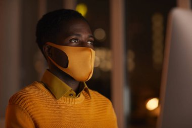 Ofiste maske takan çağdaş Afro-Amerikalı bir adamın yan görünüm portresi. Ekranla aydınlatılırken, boşluğu kopyala
