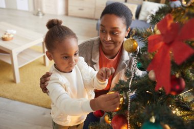 Güzel Afro-Amerikalı bir kızın portresi Noel ağacını süslüyordu mutlu bir annenin gülümsemesiyle evin içinde.