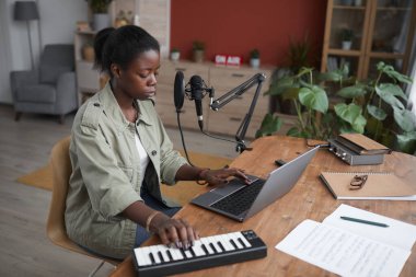 Ev kayıt stüdyosunda müzik besteleyen Afro-Amerikalı genç bir kadının yüksek açılı portresi.