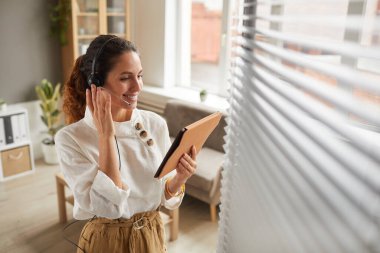 İnternetteki toplantı sırasında kulaklık takan ve dijital tablet tutan gülümseyen iş kadınının yüksek açılı portresi, boşluğu kopyala