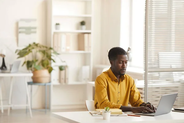 オフィスの最小限のインテリアでデスクで作業しながら ラップトップを使用して現代アフリカ系アメリカ人男性で広い角度ビュー コピースペース — ストック写真