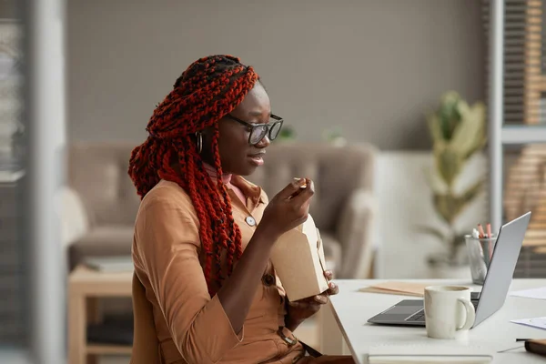 仕事のフォームホームオフィス コピースペースを楽しみながら テイクアウトランチを食べ ラップトップ画面を見て若いアフリカ系アメリカ人女性のサイドビューの肖像画 — ストック写真