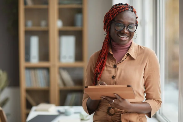 オフィスの窓のそばに立っている間 デジタルタブレットを保持し 陽気に笑顔現代アフリカ系アメリカ人女性のウエストアップ肖像画 コピースペース — ストック写真