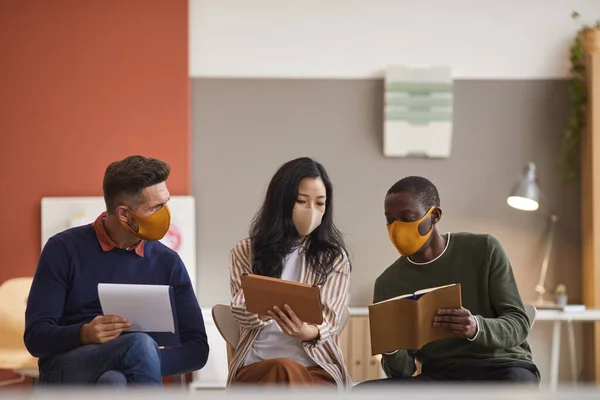 Multi-ethnic group of three business people wearing face masks while discussing project in office