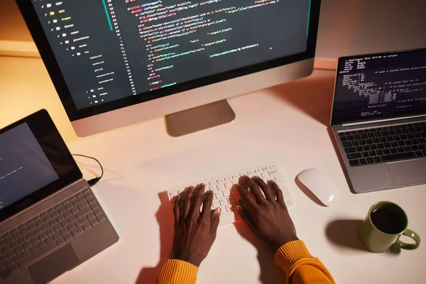 Top view close up of unrecognizable African-American man writing code while working with multiple computer screens, copy space