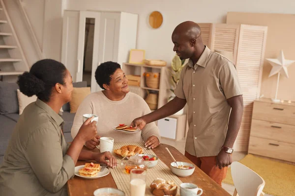 Warm toned portrait of happy African-American family enjoying breakfast at home in cozy interior