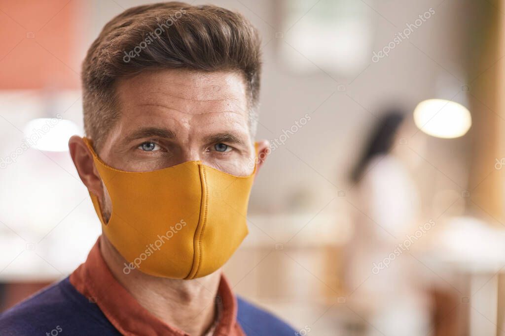 Close up portrait of handsome mature man wearing mask and looking at camera while standing in office interior, copy space