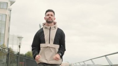 Orta yaşlı, çekici, beyaz, spor giyimli bir adamın şehirde sedyede koştuğu orta boy bir fotoğraf.