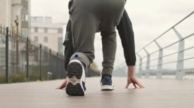 Atletik orta yaşlı, beyaz, spor elbiseli ve spor ayakkabılı bir adamın güzel bir şehirde setin içinde koşuşmasının arka görüntüsü.