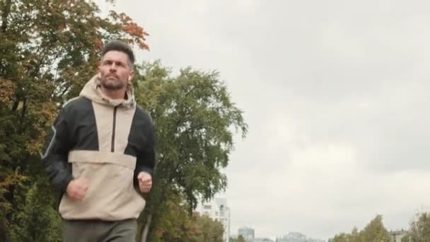 公園で走っているスポーツウェアや無線イヤフォンを身に着けている中年の白人男性の中ショット — ストック動画