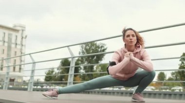 Geniş açılı kıvırcık saçlı, beyaz saçlı, modaya uygun spor giysiler giyen ve şehirde bacaklarını iskelede açan spor ayakkabılı bir kadın.