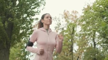 Spor kıyafetleri giymiş beyaz bir kadının parkta koşarken orta boy bir fotoğrafı.