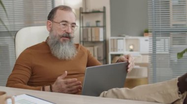 Öfkeli üst düzey Kafkasyalı iş adamı ofiste bacakları masanın üstünde oturuyor, bilgisayarında video görüşmesi yapıyor, öfkeyle kapatıyor, gözlüklerini çıkarıyor, sonra onları atıyor ve kameraya bakıyor.