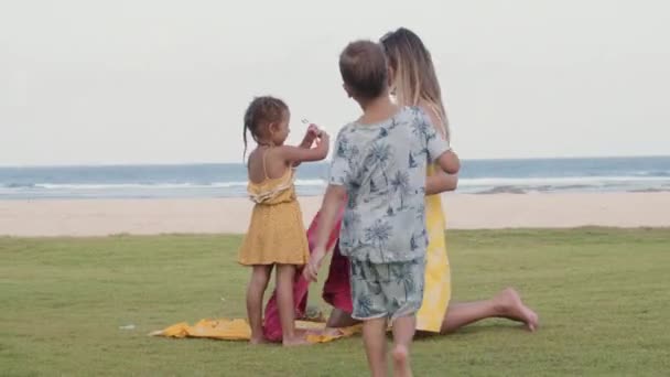 在与她的小女儿交谈的同时 拍摄了许多白种人年轻的长发女子准备离开海滨 然后白人男孩拥抱她 然后拥抱女孩 — 图库视频影像