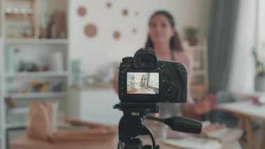 Mutfakta video bloğu çekmek için kamera ve ışıklar ayarlandı. Önlük ve lavalier mikrofon takan, masanın yanında duran, gülümseyen ve takipçilerle konuşan bulanık kadının beline kadar.