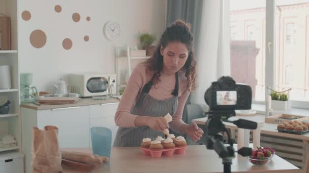 在厨房里装饰松饼的白发苍苍的小女孩拍下了一张中等稳定的照片 在她面前的摄像机前谈论这个问题 以便进行视频教学 — 图库视频影像