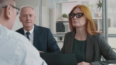 Orta yaşlı beyaz kadın işe alım müdürünün göğsü kabarmış yaşlı erkek meslektaşının yanında oturuyor, tanınmayan iş adayıyla konuşuyor, sonra da tüm mülakata katılanlar el sıkışıyor.