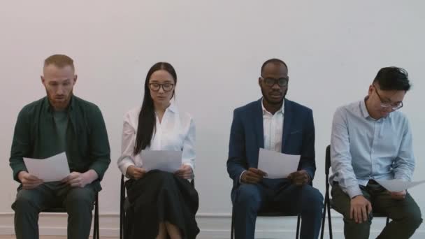 廊下に椅子に座っている4人の多様なせっかちな人々の中長期ショット 手で履歴書を保持 インタビューのための若いアジアの女性候補者を招待認識できないマネージャー — ストック動画