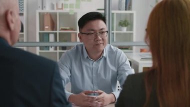 Kendine güveni tam Asyalı genç bir adamın iş görüşmesinde, tanınmayan iki işe alım yöneticisiyle konuşması, sonra yukarı bakıp kameraya gülümsemesi.