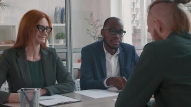 İki etnik çeşitliliğe sahip işe alım yöneticisinin orta ölçekli yakın çekimi konferans odasında masasında otururken, tanınmayan bir iş adayıyla görüşüyor.