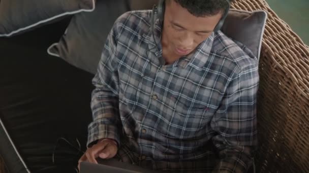 반바지 헤드폰을 아시아 청년이 무릎에 랩탑을 소파에 고객과 온라인상에서 상담하는 — 비디오