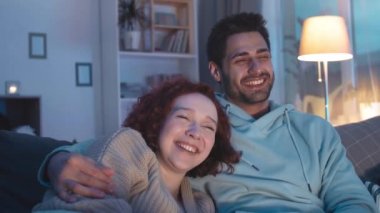 Çoklu etnik çeşitlilikte romantik partnerlerin yakın plan çekimleri. Geceleri kanepede kıvrılıp görünmez televizyon izliyor, gülüyor, Kafkas ırkından genç bir adamı kucaklıyor.