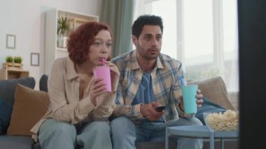 Orta uzunlukta romantik bir çift oturma odasında oturmuş konuşuyor, televizyon izliyor, kamışla kağıt bardaktan meşrubat içiyor.