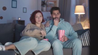 Oturma odasındaki kanepede oturup, evde televizyon seyreden patlamış mısır yiyen, filmden korkan, geri sıçrayan çok ırklı romantik partnerlerin düzenli çekimi.