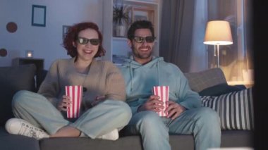 Nilüfer çiçekli kızıl saçlı beyaz bir kadının yanında oturan, elinde patlamış mısır kutuları olan, 3D gözlüklü, film izlerken kahkahalar atan...