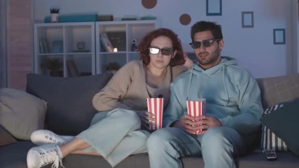 跟踪一对戴3D眼镜的年轻夫妇 坐在客厅的沙发上 看电影 把爆米花撒在自己身上 然后大笑 — 图库视频影像