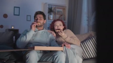 Orta uzunlukta, melez bir adam ve kızıl saçlı beyaz bir kız dairede oturuyor, sinmiş, kutudan pizza yiyor, görünmez TV 'de korku filmi izliyor, sonra da gülüyor.