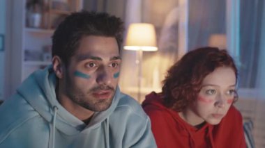 Gece kanepede oturup maç izleyen, takımının kazanmasından heyecan duyan, Kafkasyalı kız hayal kırıklığına uğramış, karışık ırk hayranlarının yakın çekimi.