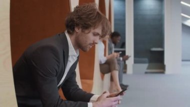 Kızıl Kafkas işadamlarının modern ortak çalışma sahasında ellerinde telefonla oturup kameraya bakarken genç bir adam ve kadının arka planda telefon kullanması.