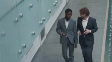 Afrika ve Kafkasyalı iş adamlarının şık takımlar giyip iş merkezi koridorunda sohbet etmelerinin yüksek açılı görüntüsü.