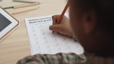 Masanın başında oturan, kağıt kağıtlara yazı yazan, toplama problemlerini çözen, ikinci sınıf için matematik ödevi yapan tanınmayan öğrencilerin omuzlarının üstünden yüksek açı.