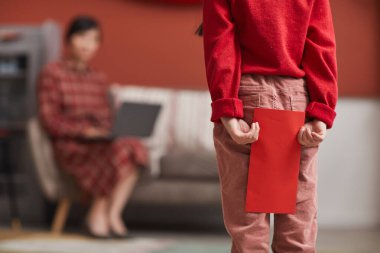 Tanımlanamayan Çinli bir kızın annesinin önünde elinde kırmızı bir zarf tutarken çekilmiş yatay göbek fotoğrafı.