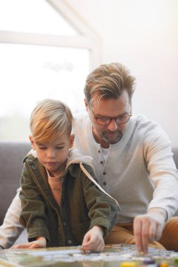Vertical portrait of modern mature father playing board game with cute son together at home