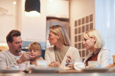 Portrait of modern happy family enjoying breakfast together sitting at table in cozy kitchen interior, parents with two children, copy space