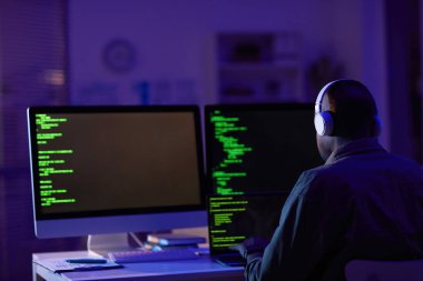 Kulaklık takan profesyonel yazılım geliştiricisinin ofiste tek başına oturup bilgisayar üzerinde çalışıp yeni kodlar oluşturduğu arka plan görüntüsü