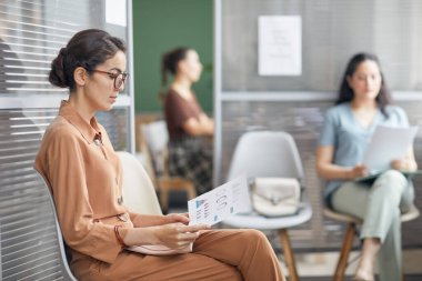 Zarif genç iş kadınının yan görünüm portresi çizelgelere bakıyor ve ofiste sırada beklerken rapor veriyor, boşluğu kopyalıyor.