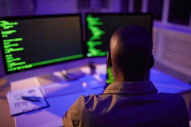 Tanımlanamayan Afro-Amerikan bilgisayar programcısının, yazılım kodu üzerinde çalışan monitörlerin önünde oturduğu arka plan görüntüsü