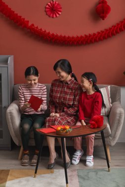 Vertical long shot of modern Chinese family consisting of mother and two daughters spending time together preparing for New Year holidays clipart