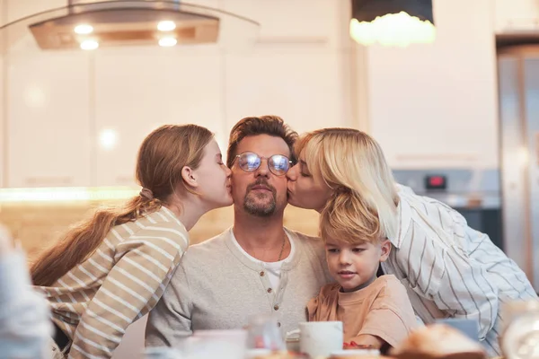 Retrato Pai Feliz Desfrutando Beijos Três Crianças Enquanto Sentado Mesa — Fotografia de Stock