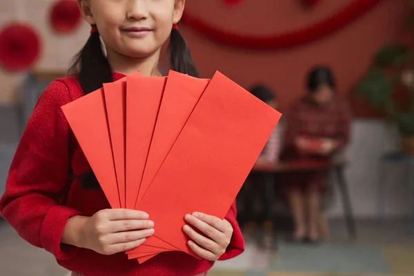 Head cropped shot of little Chinese girl with two ponytails hairstyle holding bunch of handmade red envelopes