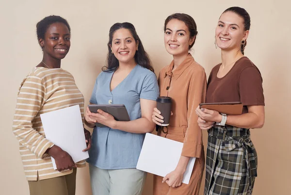 Multi-ethnic group of four young businesswomen looking at camera while standing by wall in office