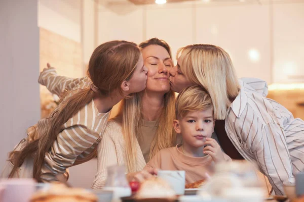 Retrato Mãe Feliz Desfrutando Beijos Três Crianças Enquanto Sentado Mesa — Fotografia de Stock