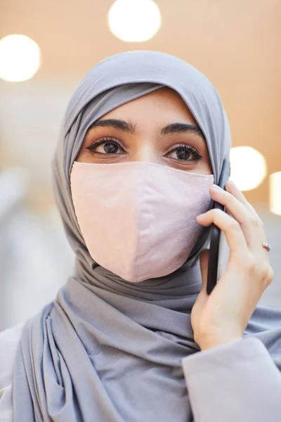 站在购物中心时 带着面具和用智能手机说话的现代中东妇女的垂直特写 — 图库照片