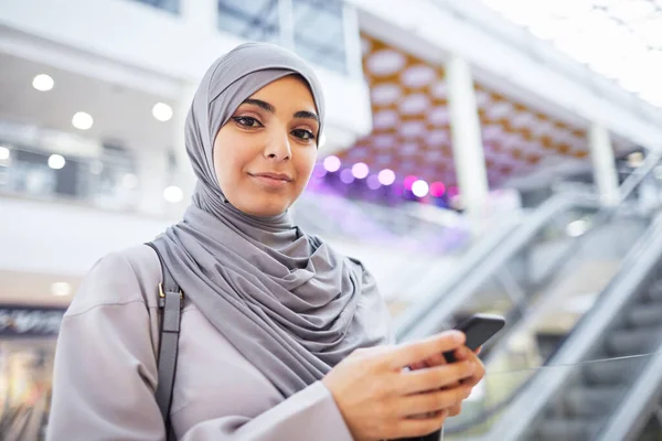 举起笑容可亲的中东女人的肖像 一边拿着智能手机 一边看着相机 一边欣赏商场购物 复制空间 — 图库照片