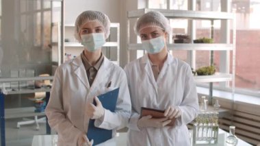 Laboratuvarda dikilen ve kameraya bakan iki beyaz kadın biyokimyacı.